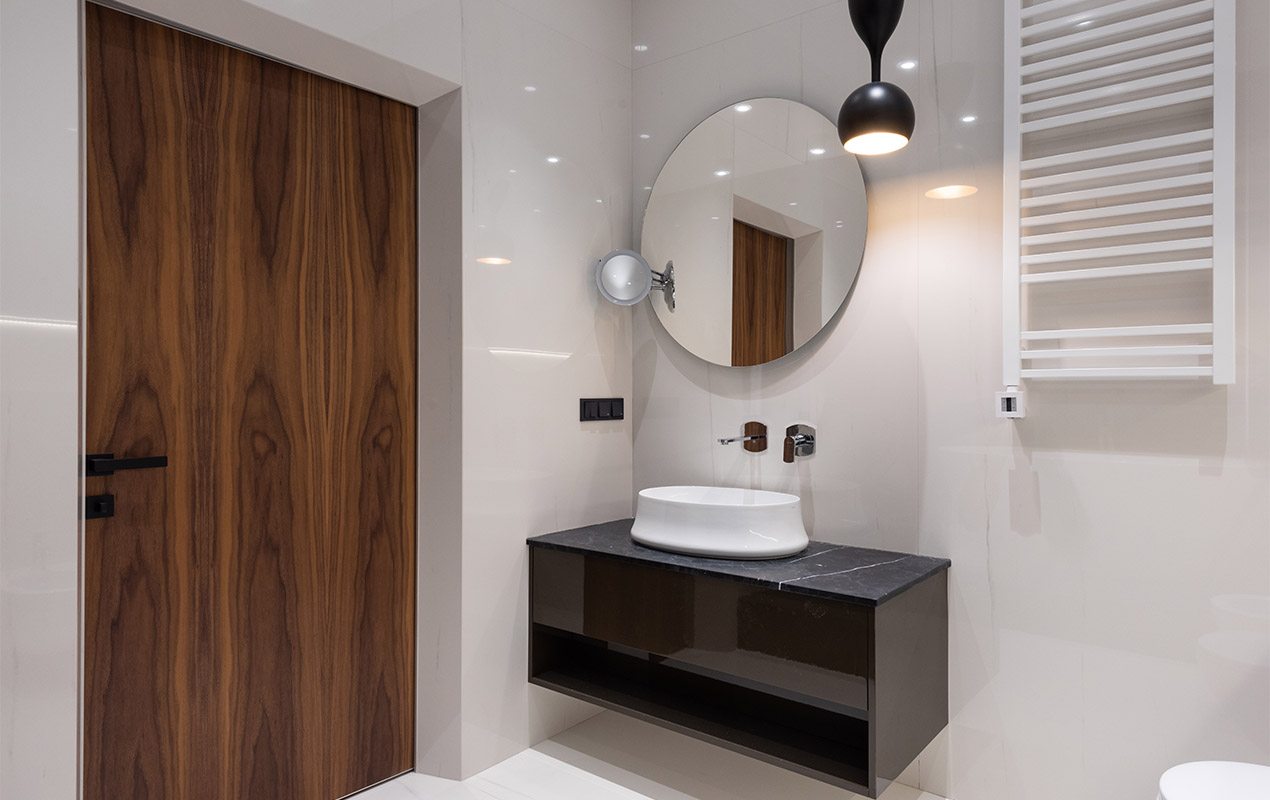 A decorated all-white bathroom with a contrasting cabinet, sink, and a round mirror