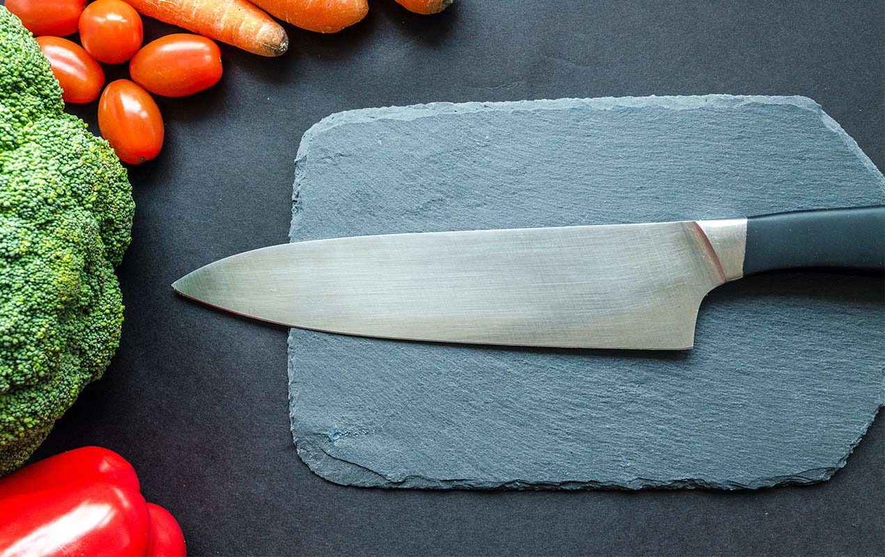 Kitchen knife on a slate board and vegetables