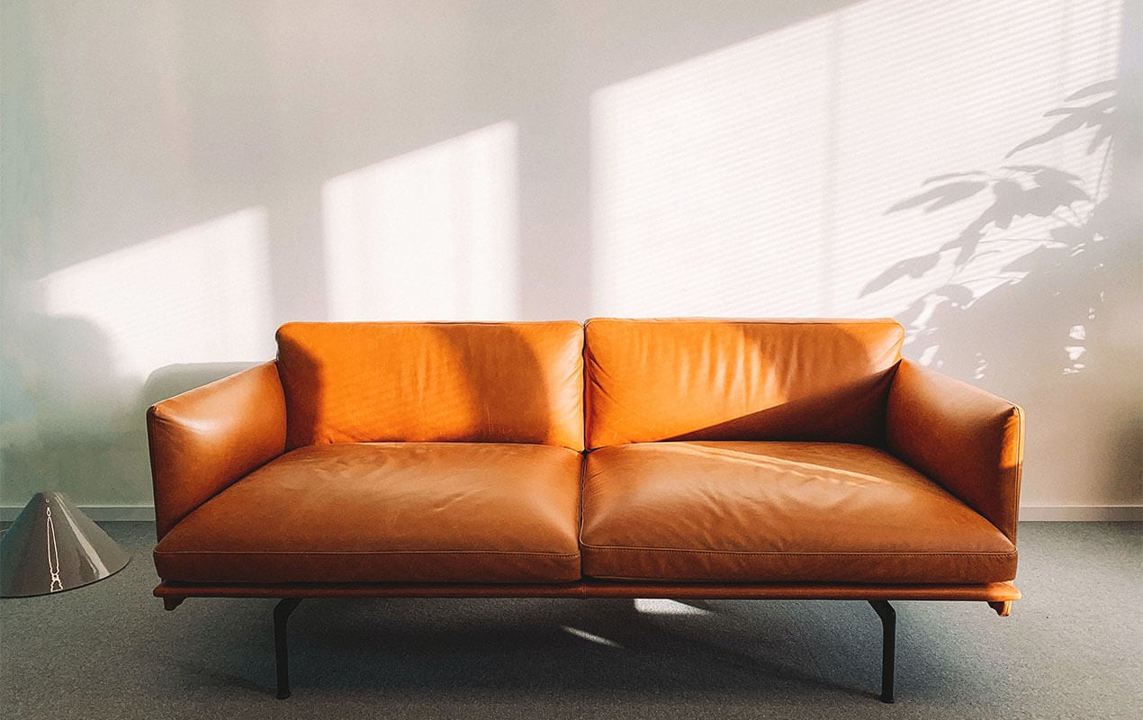 A mid century brown sofa in front of white wall.