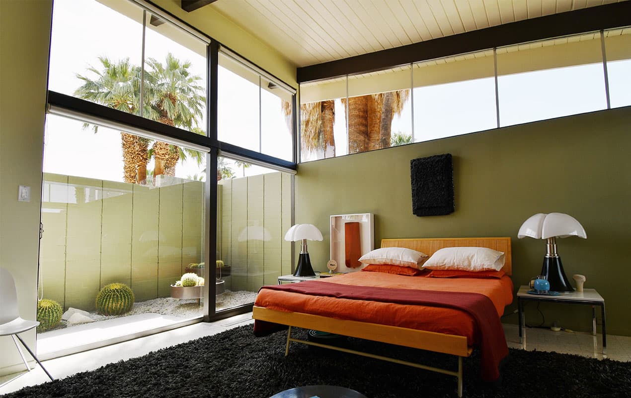 Orange bed in front of pale green walls with floor to ceiling windows