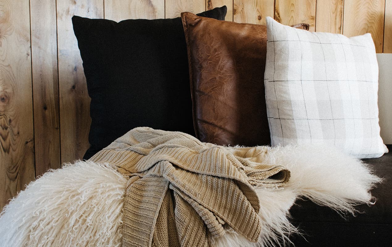 Three pillows in front of wooden wall, fur throw and wool throw