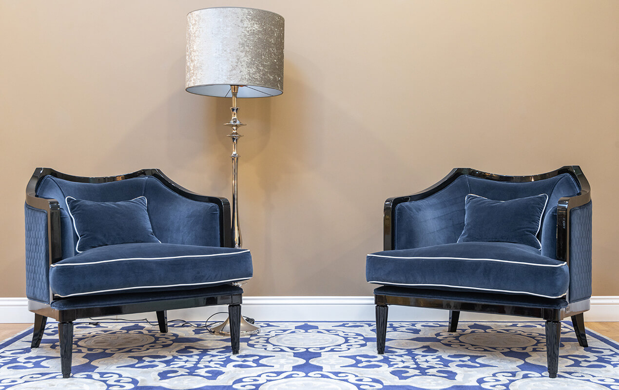 Two suede chairs on patterned rug with a floor lamp