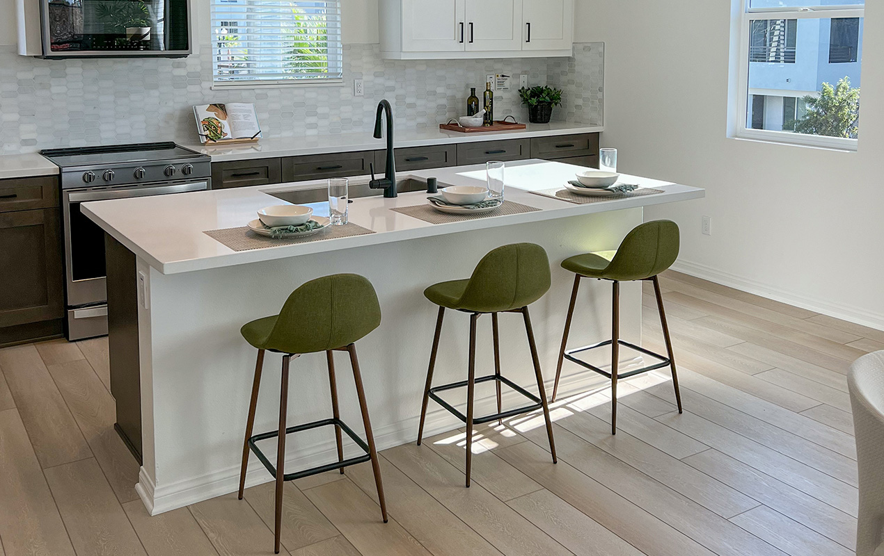 White kitchen with gray flooring and green stools by DeCasa Collections
