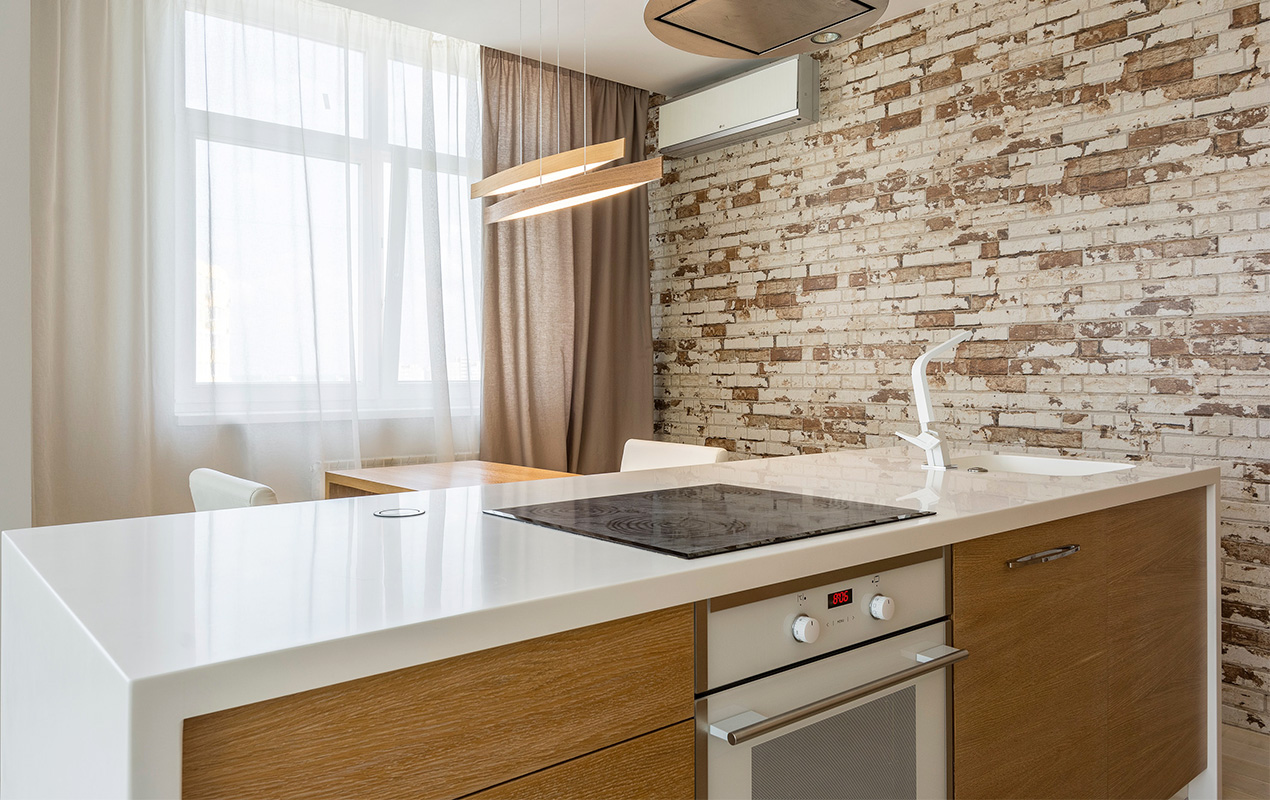 Natural kitchen design with a stone wall, brown curtain, and wood island by DeCasa Collections