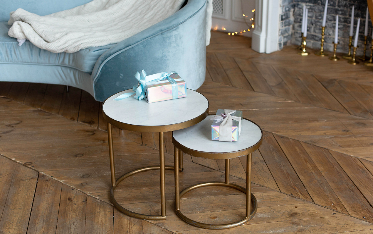 https://www.decasacollections.com/wp-content/uploads/2023/08/two-small-gold-tables-with-white-table-top-blue-chair-with-white-blanket-it.jpg